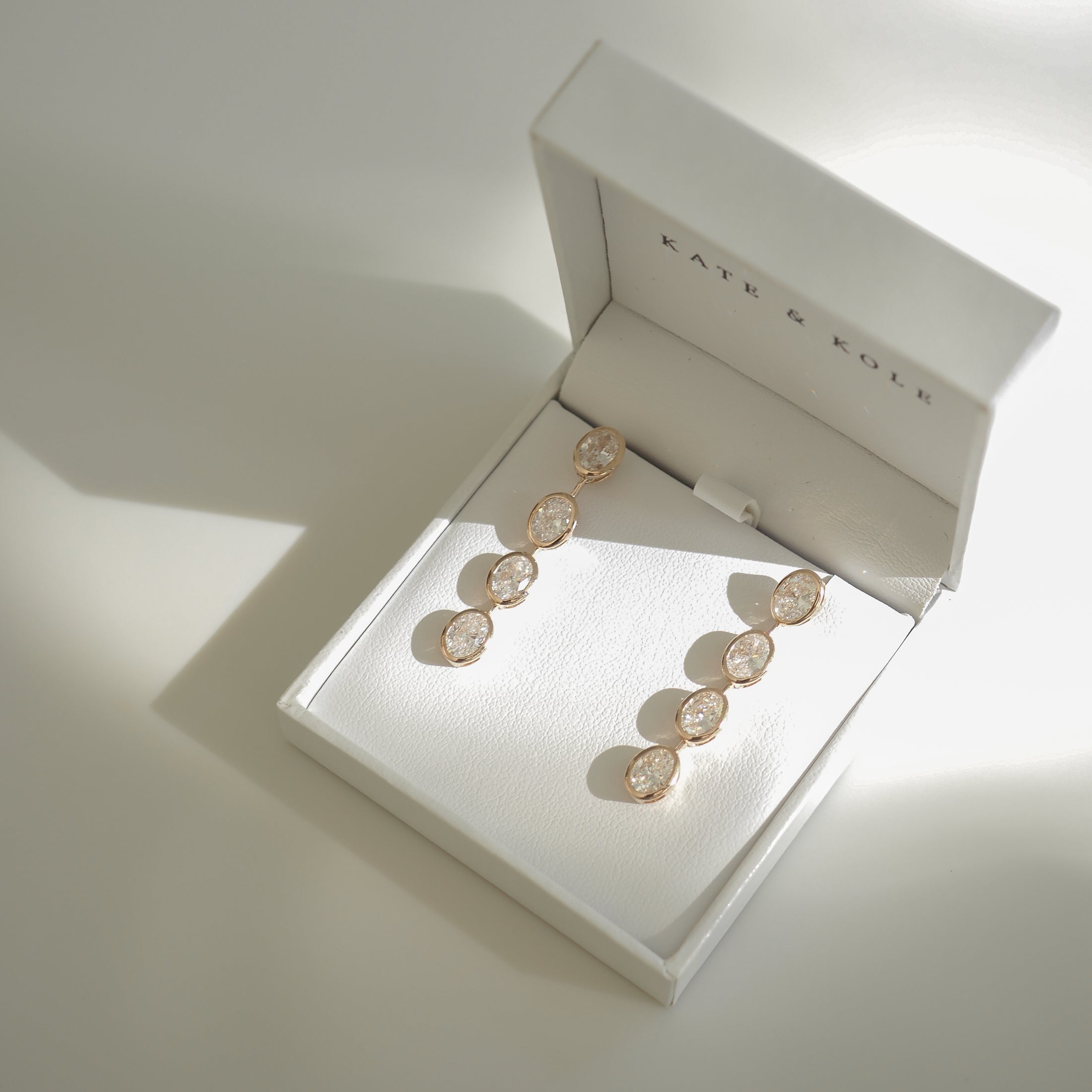 Elegant gold earrings with round gemstones displayed in a white jewellery box, casting soft shadows, exemplifying luxury fashion.