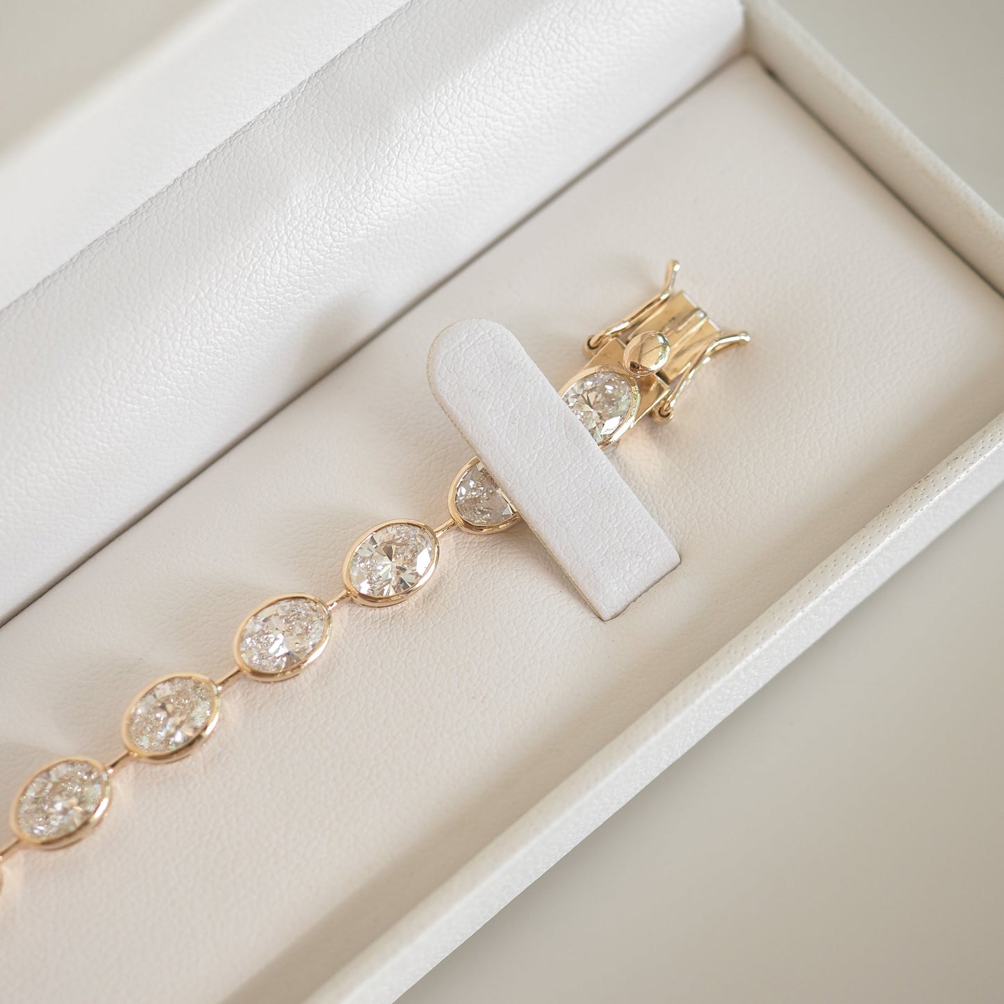 Gold bracelet with oval diamond settings in a white jewellery box. Luxurious and elegant, ideal for high-end fashion enthusiasts.