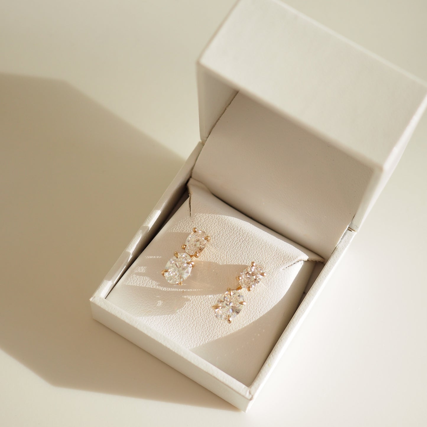 Elegant diamond earrings in a luxurious white jewellery box, illuminated by soft natural light.