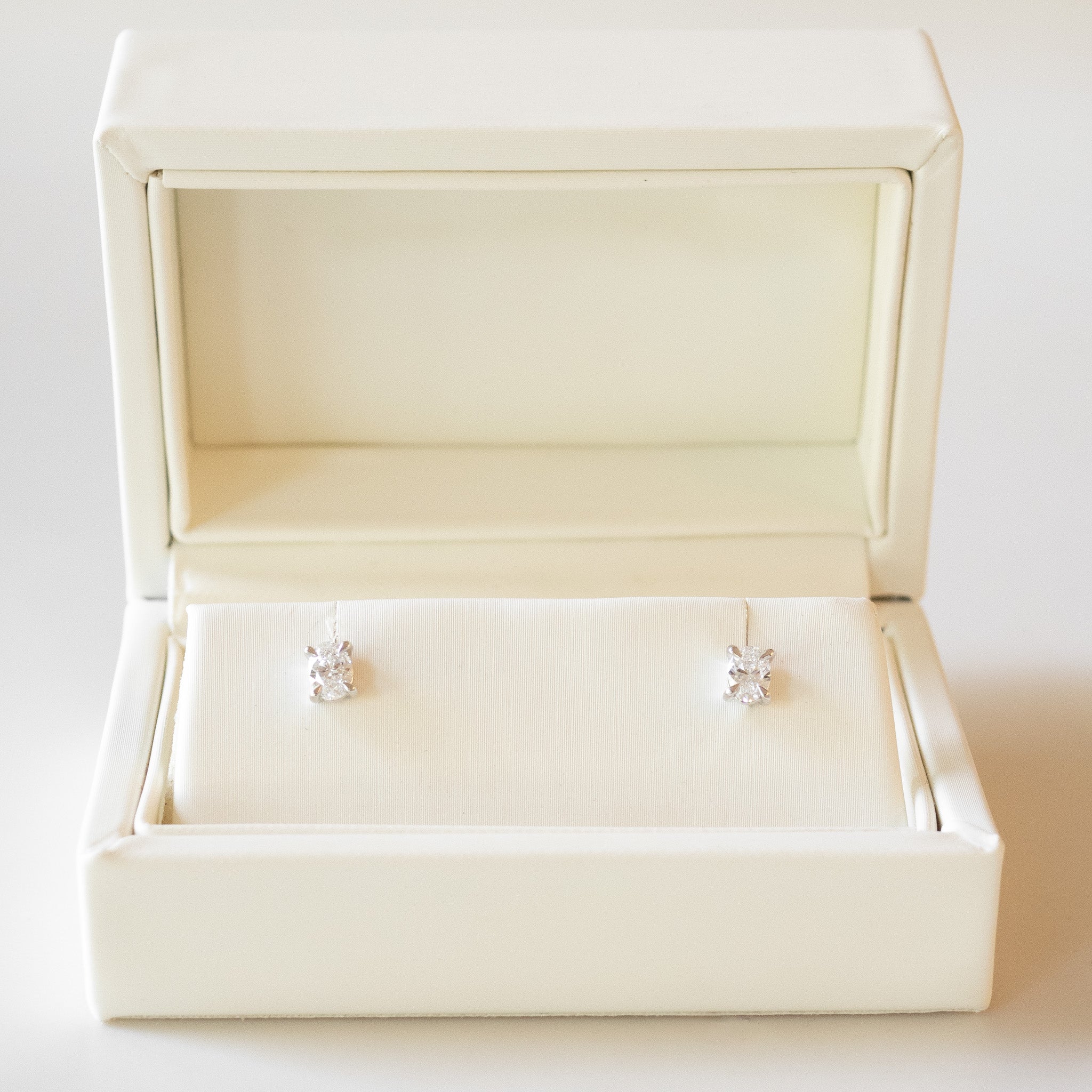 Pair of diamond stud earrings in an open cream jewelry box on a white background