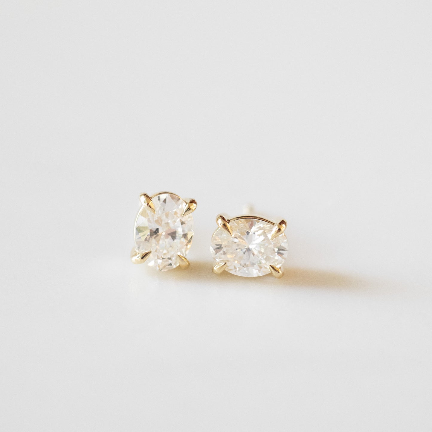 Gold stud earrings with clear gemstones on a light gray background