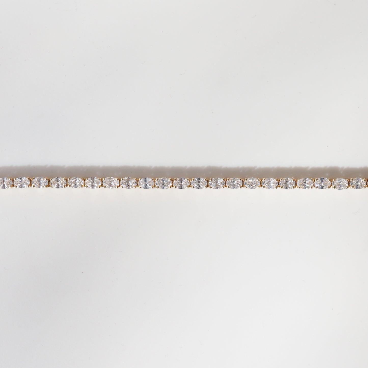Elegant diamond tennis bracelet with sparkling stones set in a fine gold band on a minimalist white background.