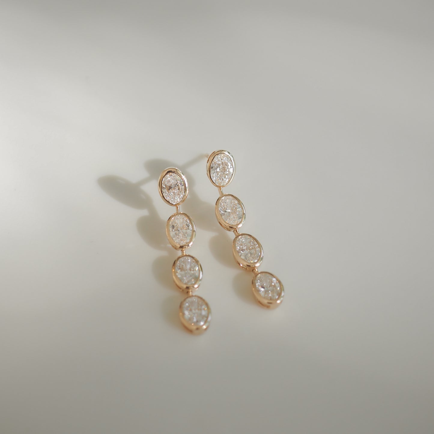 Elegant gold drop earrings featuring five oval diamonds each, set against a soft, light background, embodying luxury jewellery charm.
