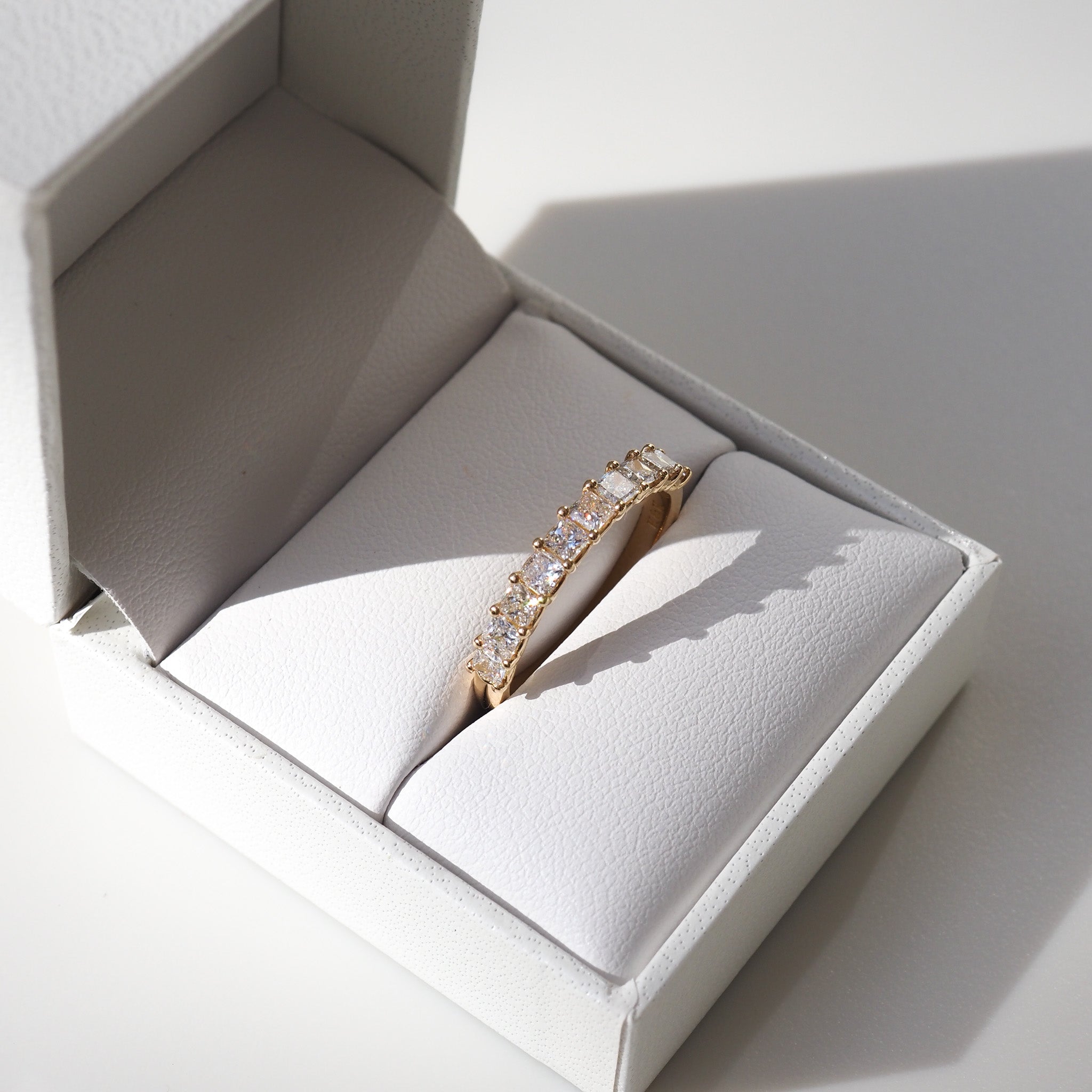 Gold diamond eternity band displayed in an open white jewellery box, casting a soft shadow. Luxurious and elegant design.