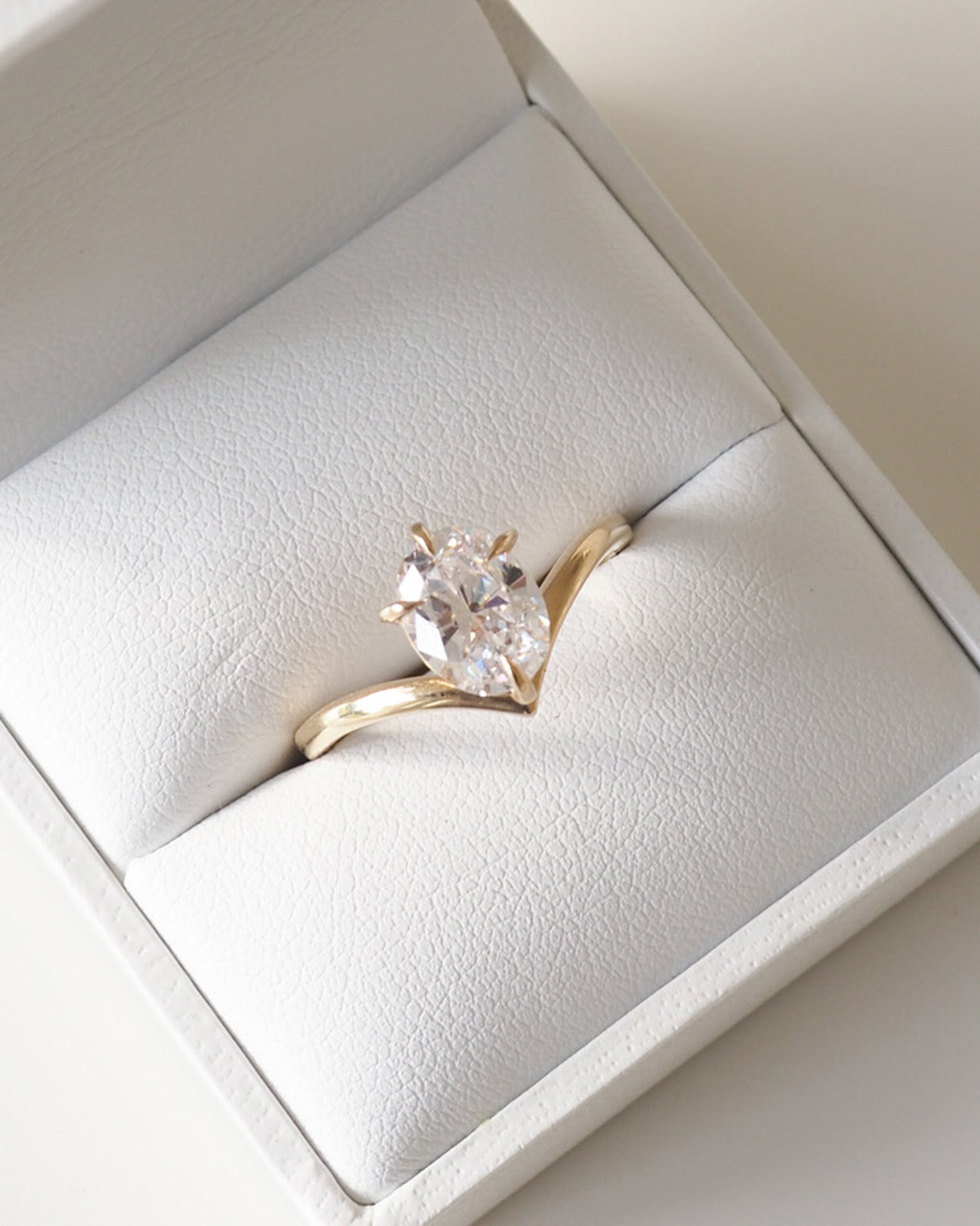 Gold ring with a pear-shaped diamond set in a white ring box, showcasing luxury jewellery design.