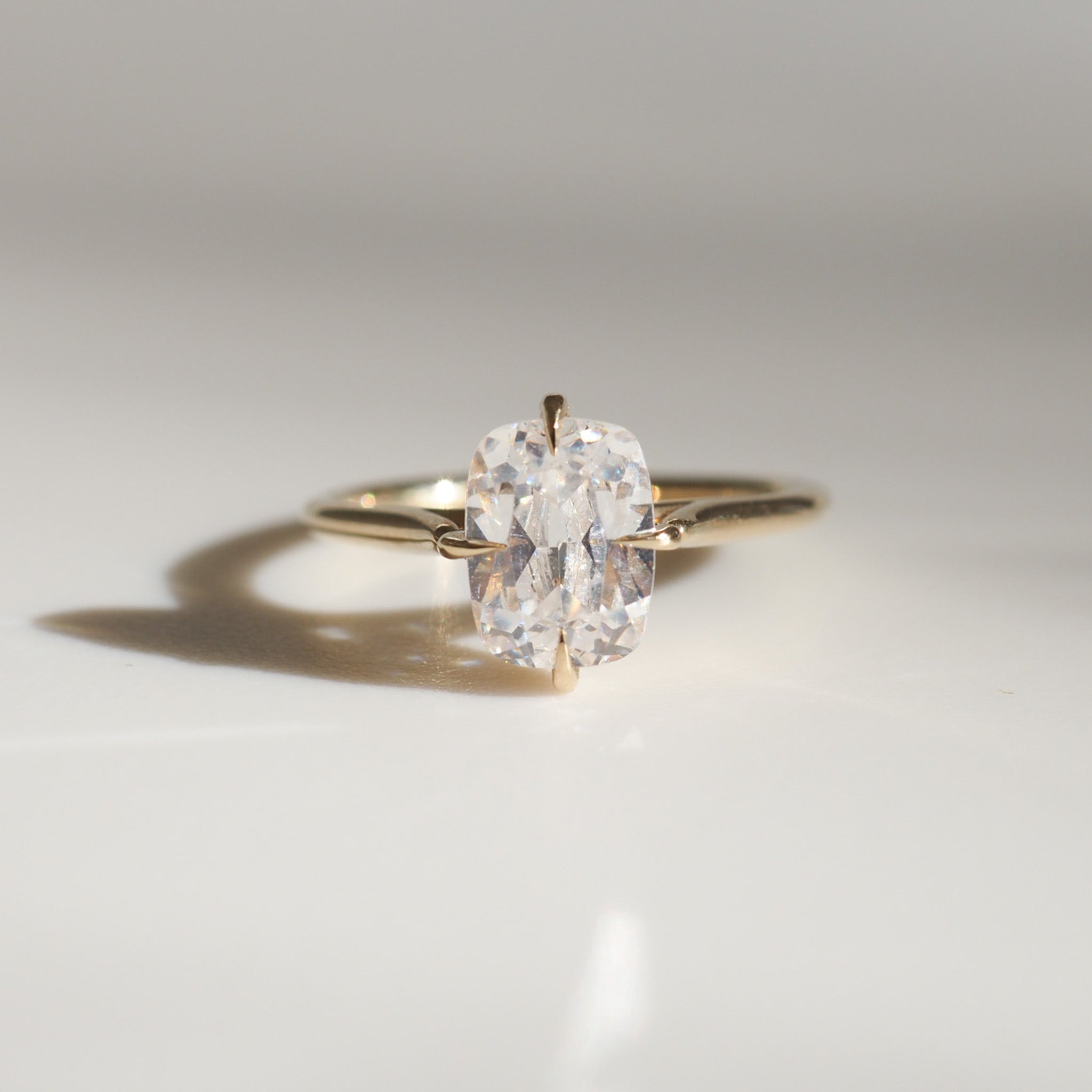 Elegant solitaire diamond ring with a gold band on a reflective surface, casting a delicate shadow. Perfect for luxury jewellery lovers.