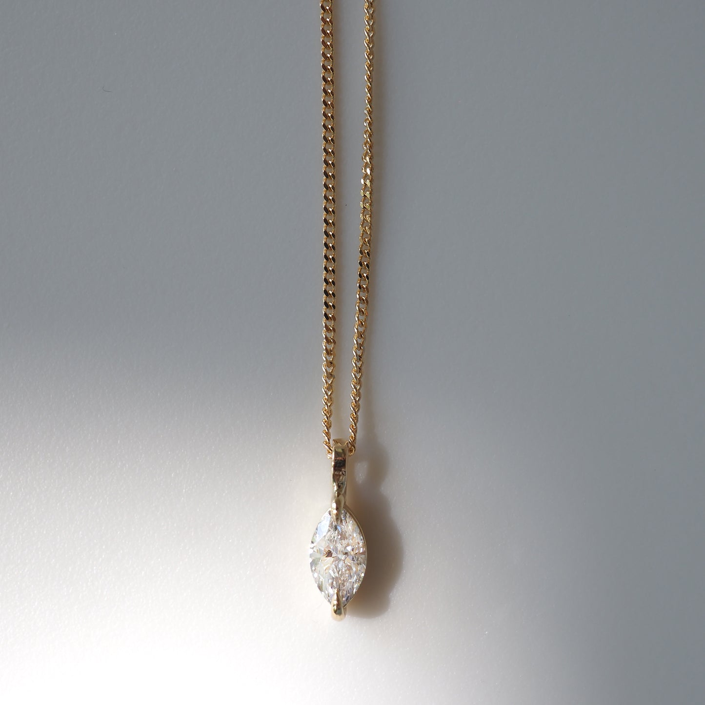Gold chain necklace with marquise-cut diamond pendant, elegantly displayed against a neutral background, showcasing luxury jewellery design.