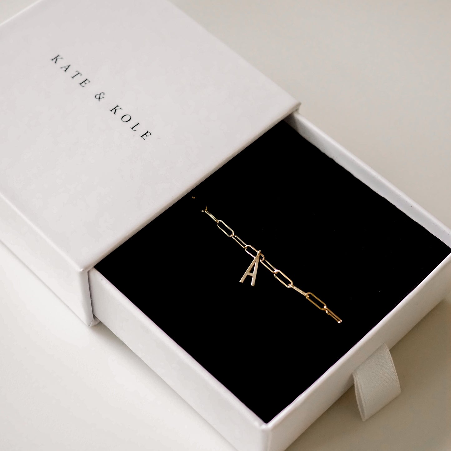 Gold chain bracelet with an 'A' charm, presented in an elegant Kate & Kole branded white box with a black interior.