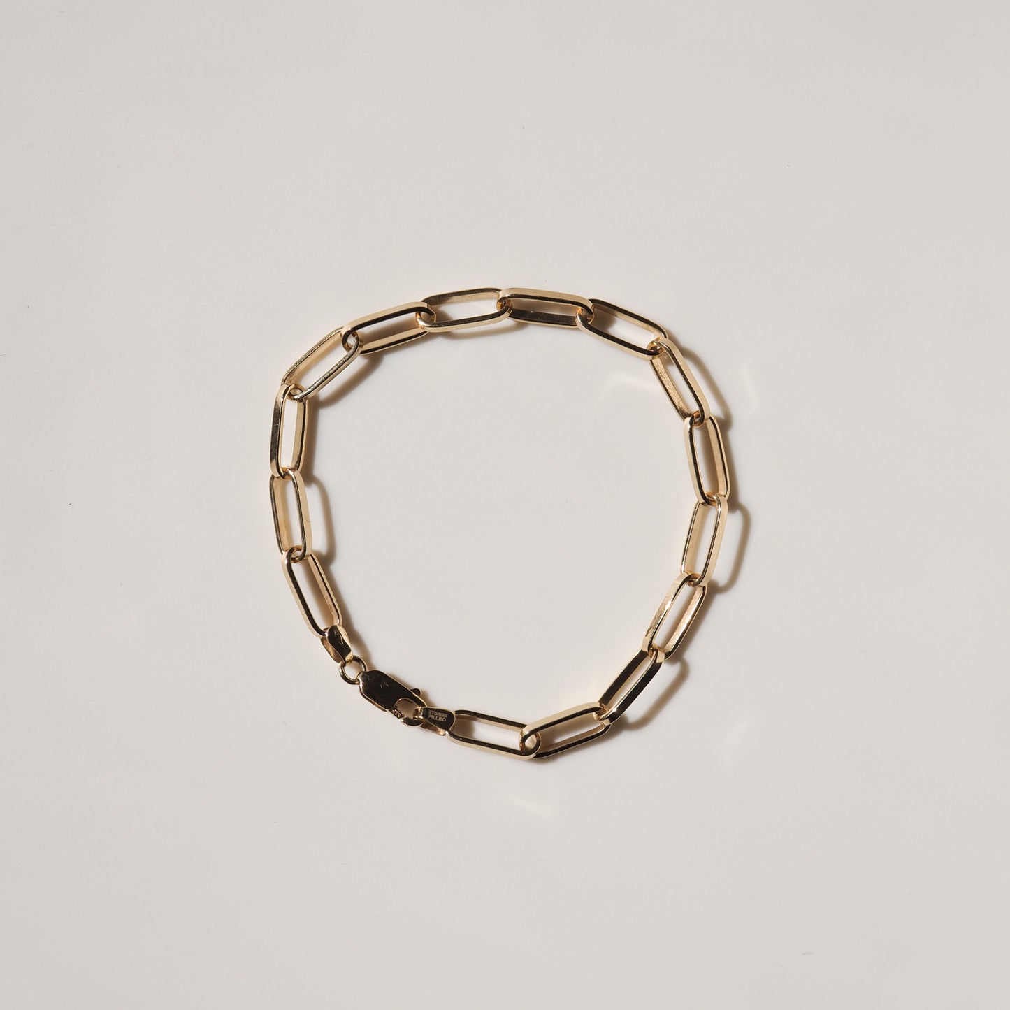 Gold link bracelet with elongated oval links and a lobster clasp on a white background. Luxurious and elegant jewellery piece.