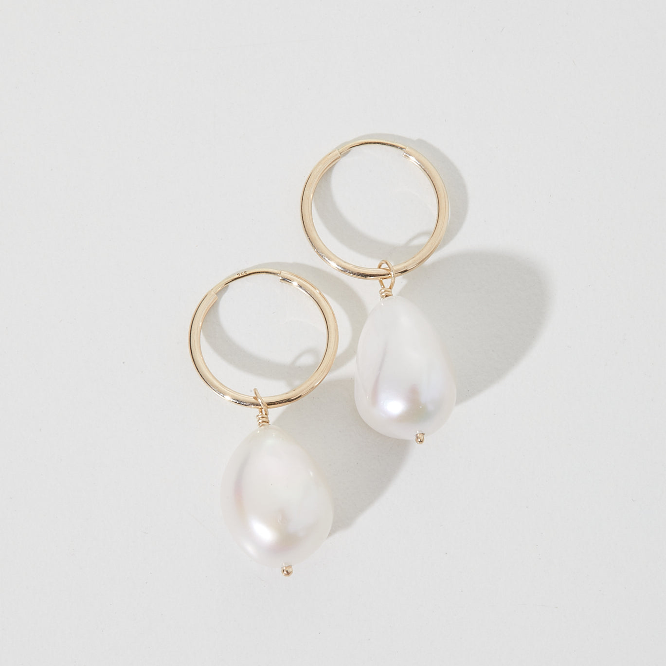 Gold hoop earrings with large, irregular white pearls on a plain background, showcasing luxury jewellery design.