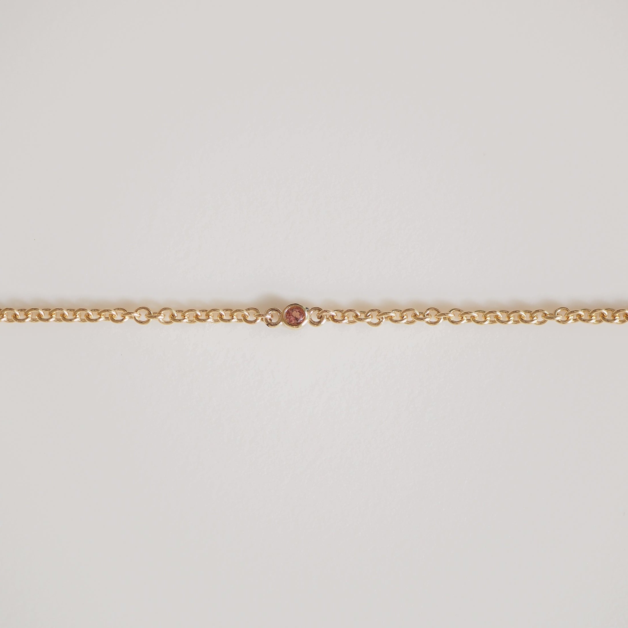 Gold chain with a single, small pink diamond in the centre. Elegant and minimalist luxury jewellery on a plain white background.