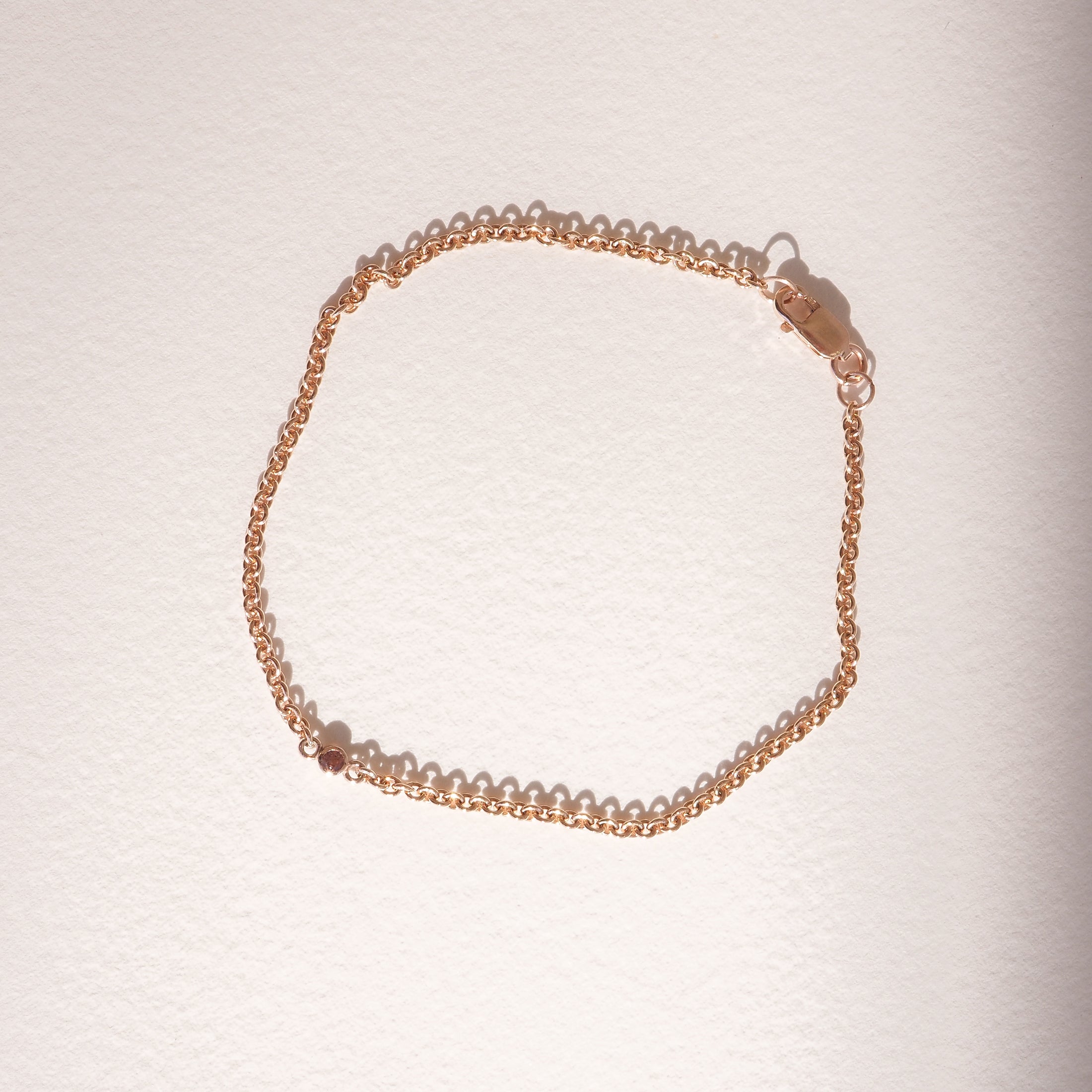Elegant gold chain bracelet with a delicate design, casting a soft shadow on a light surface. Ideal for luxury jewellery enthusiasts.