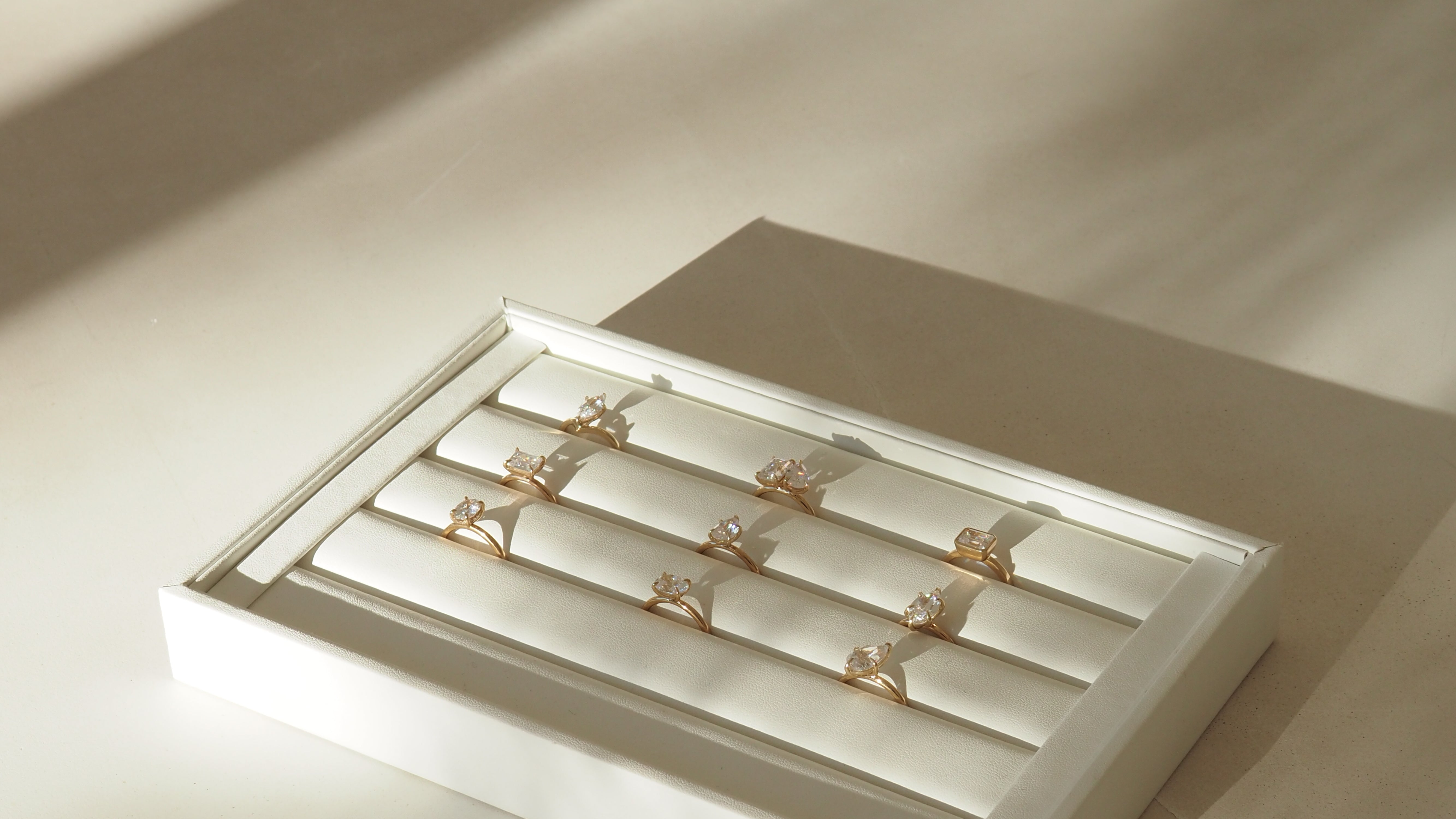 A display box with elegant gold rings, each featuring a large gemstone, neatly arranged in a sunlit setting, ideal for luxury jewellery shopping.