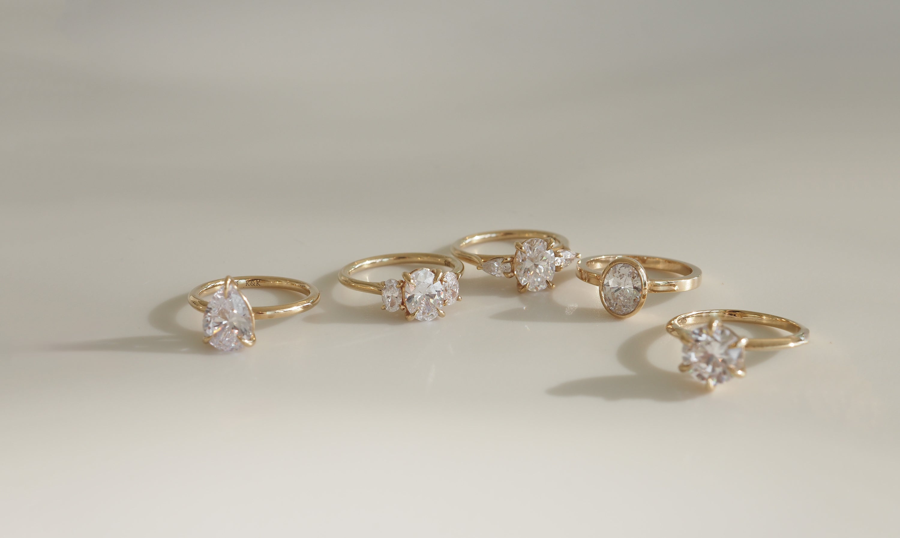 Gold engagement rings with large diamond stones, elegantly arranged on a neutral surface, showcasing luxury jewellery design.
