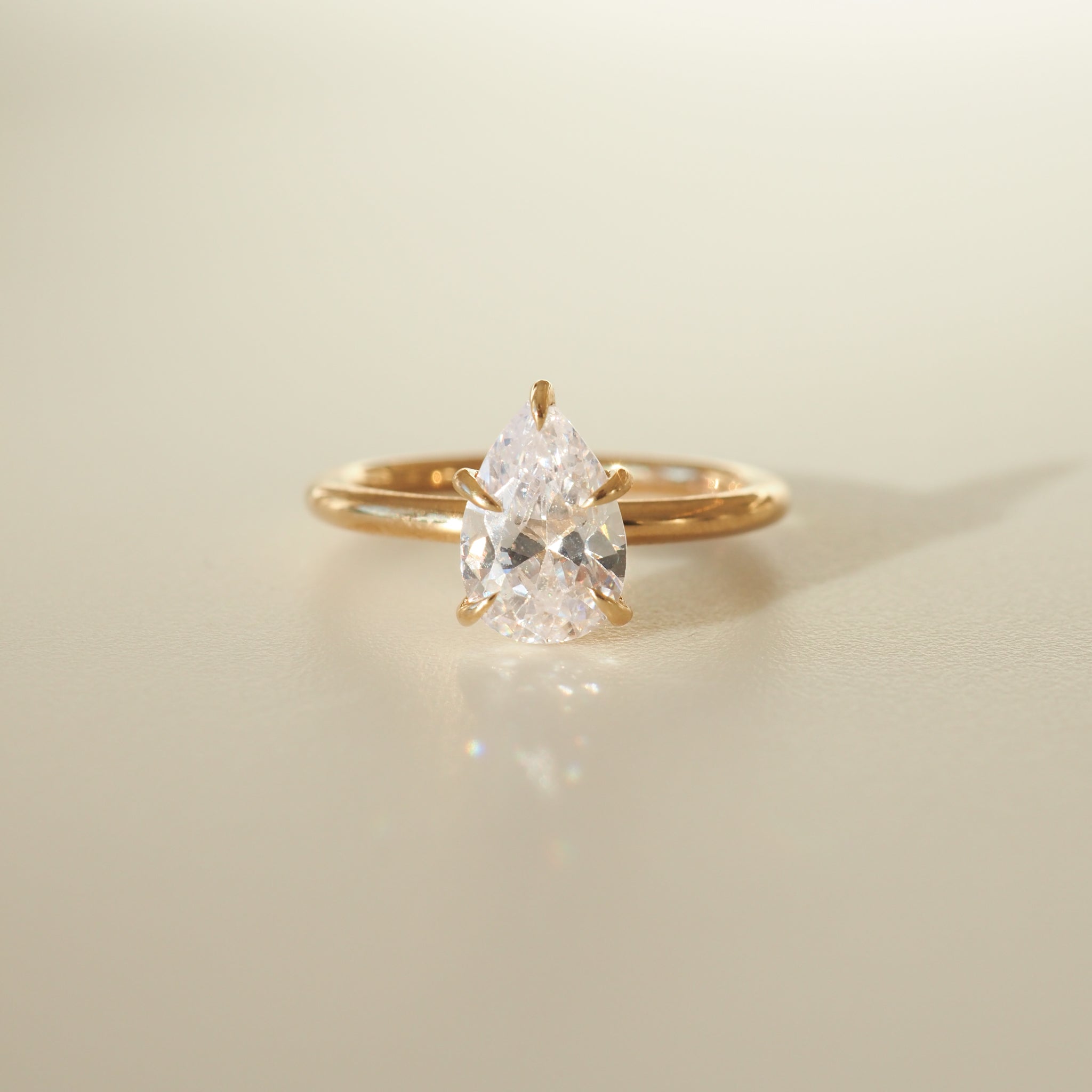 Pear-shaped diamond ring with a gold band set against a soft, light background, showcasing luxury jewellery elegance.