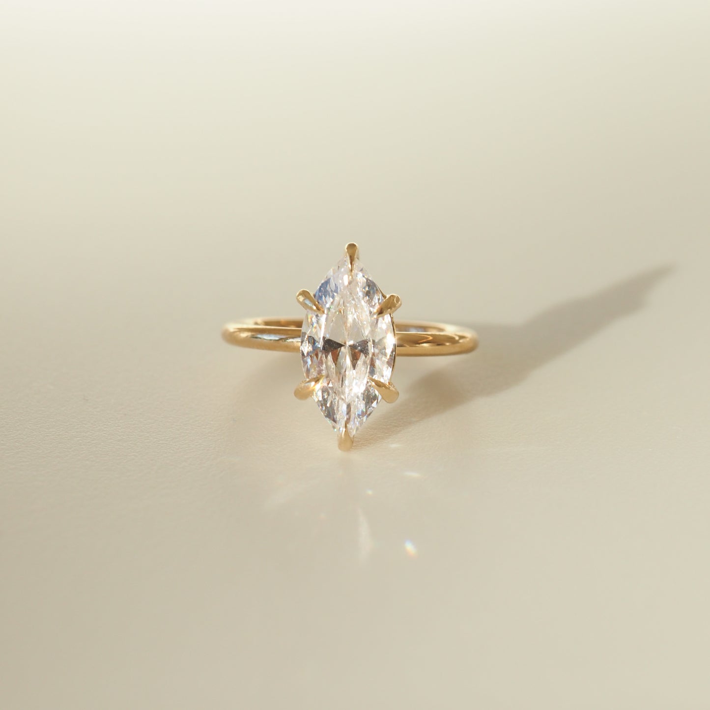 Marquise-cut diamond ring set on a sleek gold band, casting a soft shadow on a neutral background. Ideal for luxury jewellery enthusiasts.
