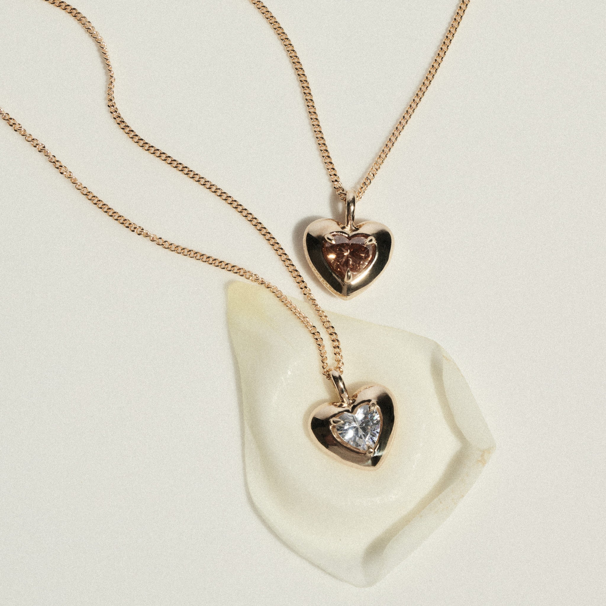 Two heart-shaped pendants on gold chains lying on a white stone surface.