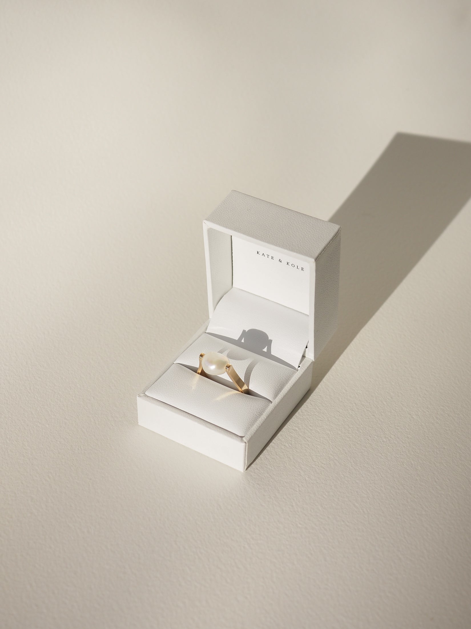 A luxurious gold ring with a large pearl set in an elegant white box on a light surface. Perfect for high-end jewellery lovers.