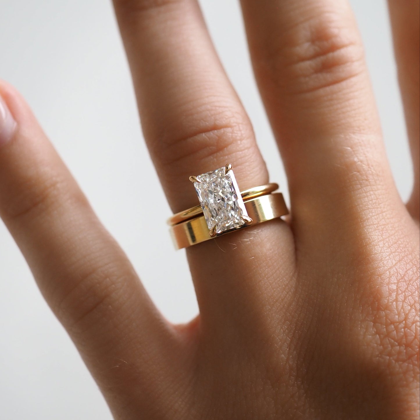 Hand wearing a gold band with a large rectangular diamond ring, showcasing luxury jewellery craftsmanship.  [text overlay: Medium with 1.5ct Rhea] [text colour: #000000]
