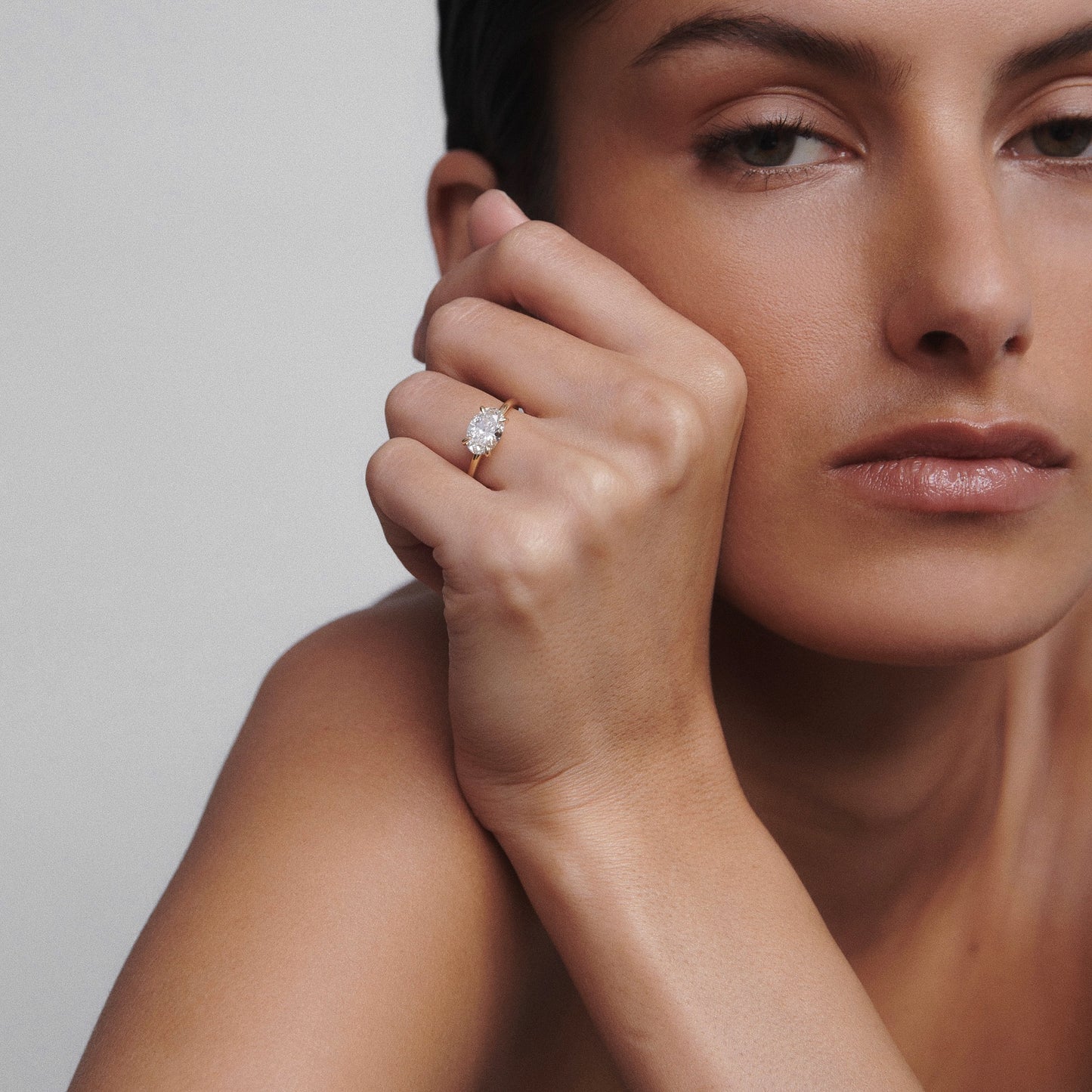 Woman with sleek hair wearing an elegant diamond ring, displayed on her finger, in a luxurious and minimalist setting.