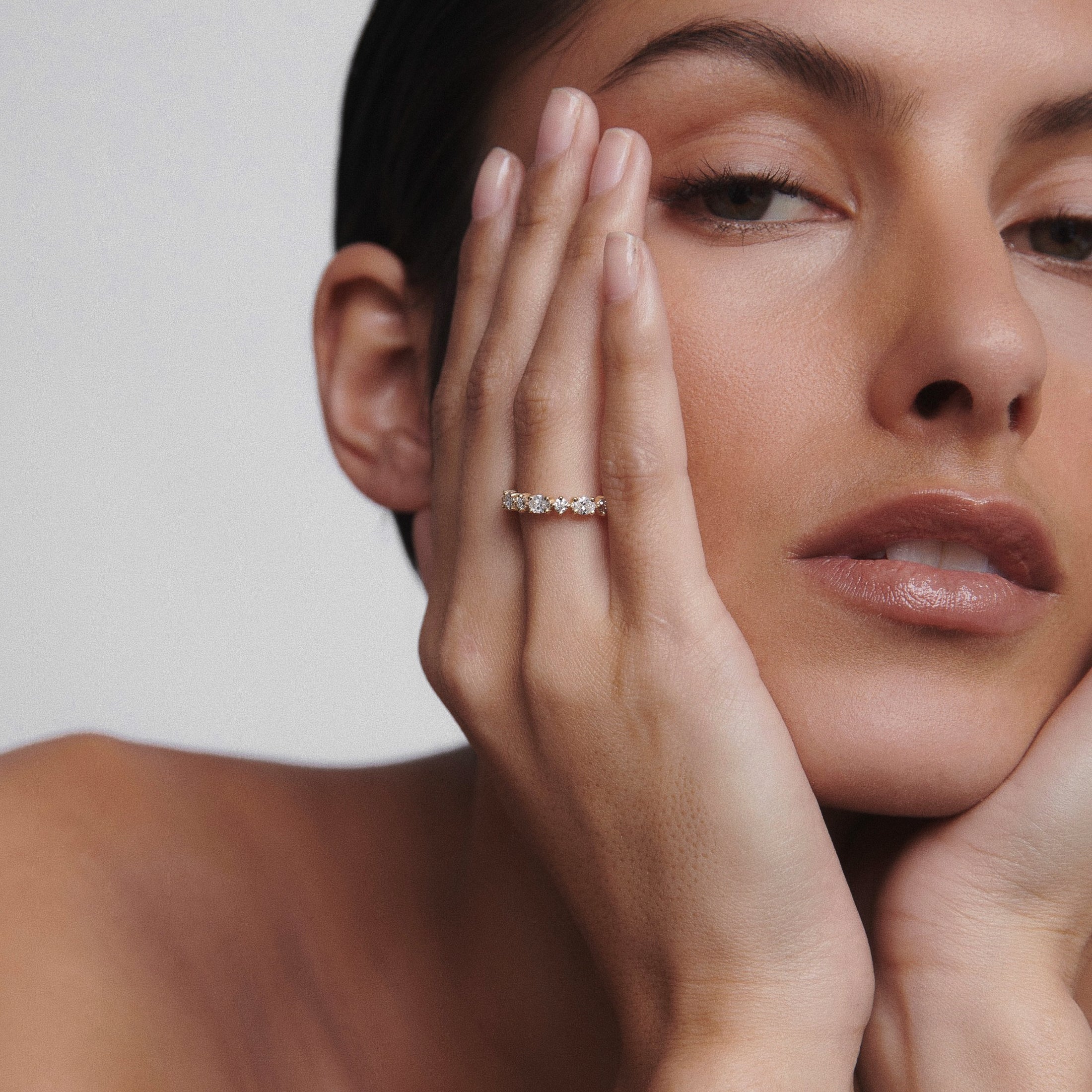 Woman wearing a luxurious diamond ring on her finger, resting her face on hands. Elegant, minimalist jewellery design.