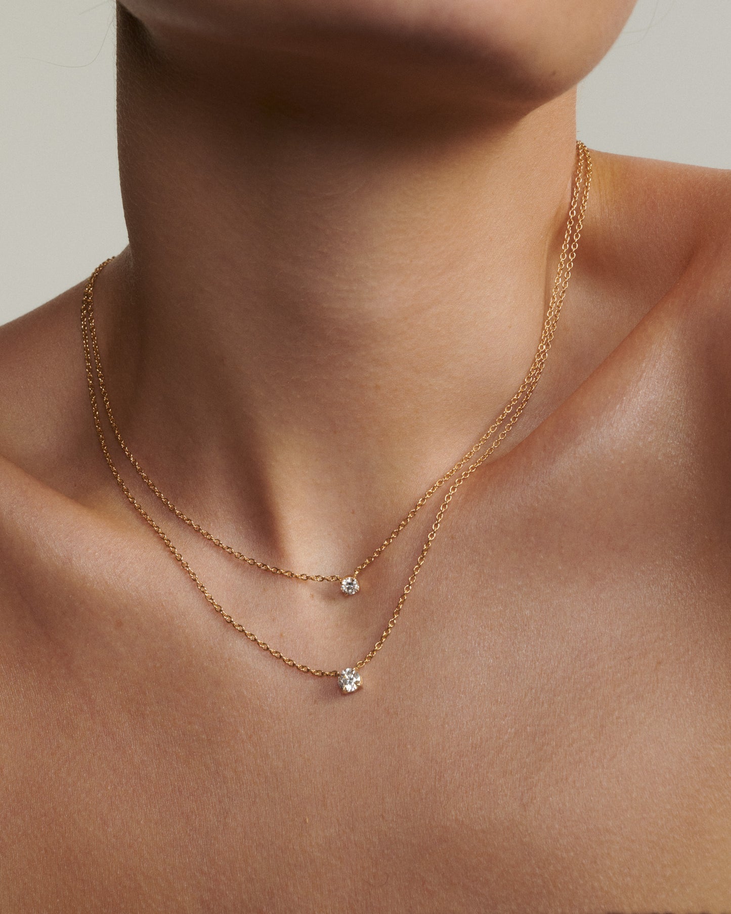 Gold necklace with small pendants on a person's neck against a neutral background