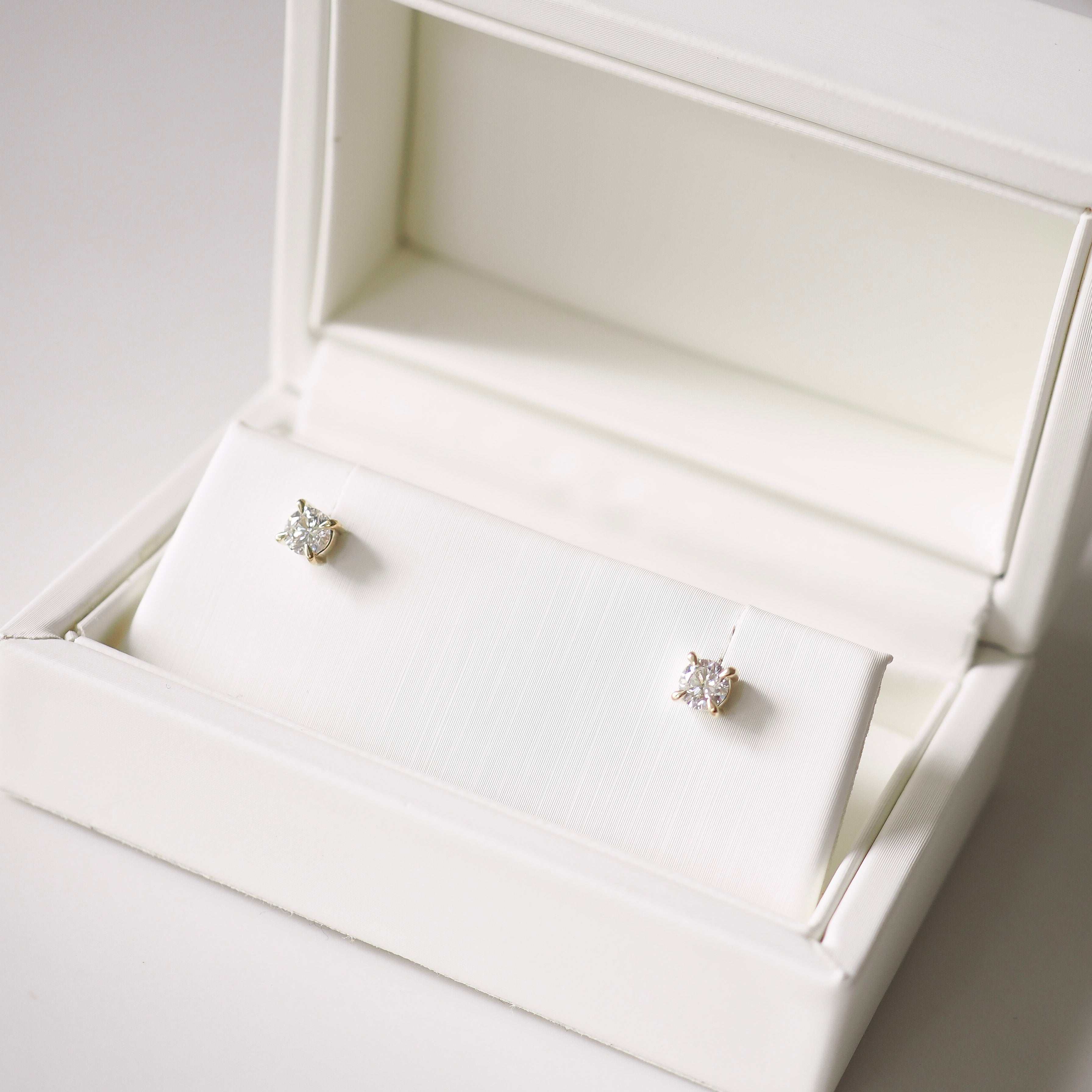 Pair of diamond stud earrings in an open white jewelry box.