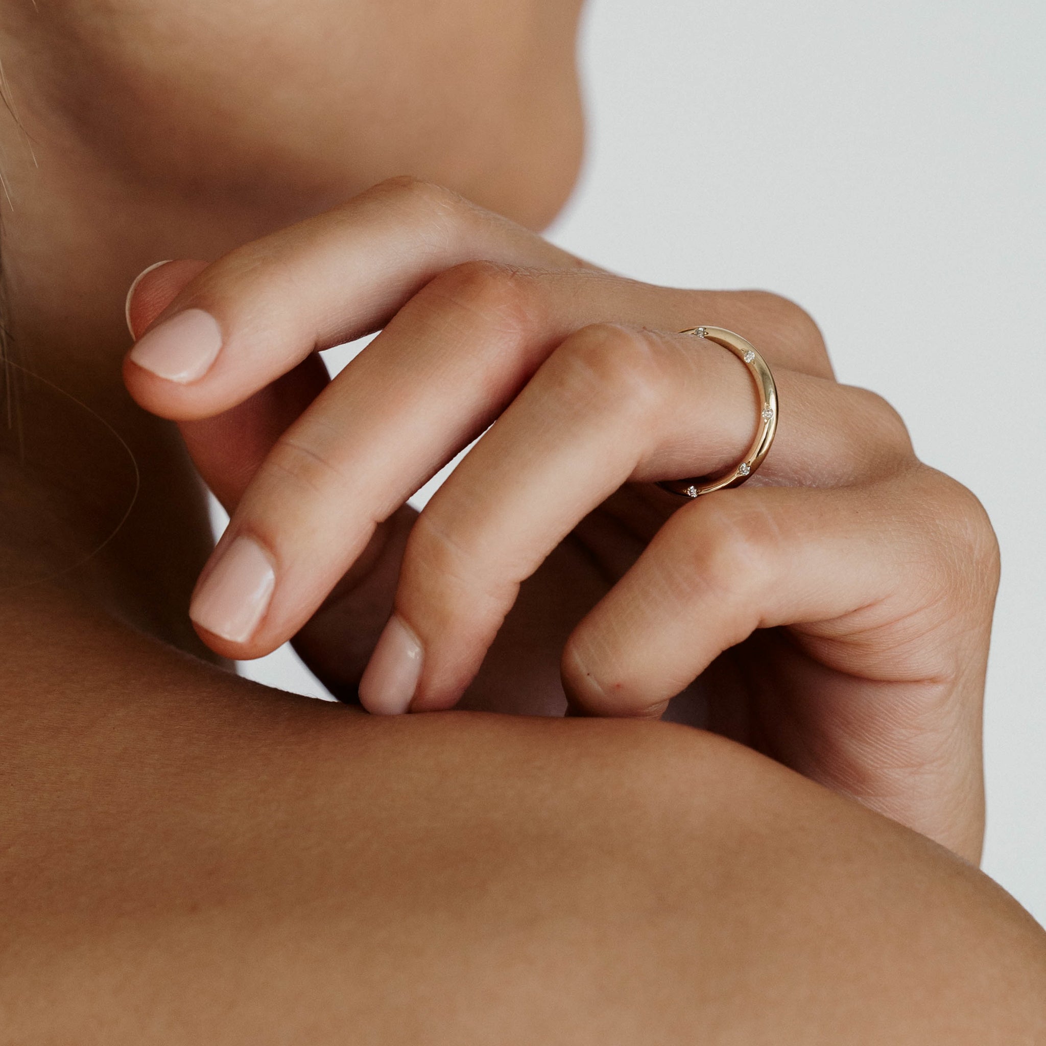 Close-up of a hand with a minimalist gold ring, resting on a bare shoulder. Elegant fine jewellery, showcasing simple luxury.