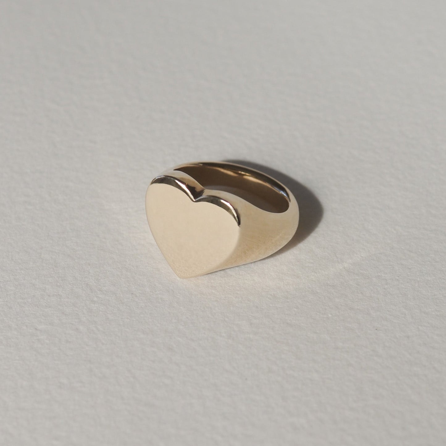 Gold heart-shaped ring on a light textured background, showcasing minimalist luxury jewellery design.