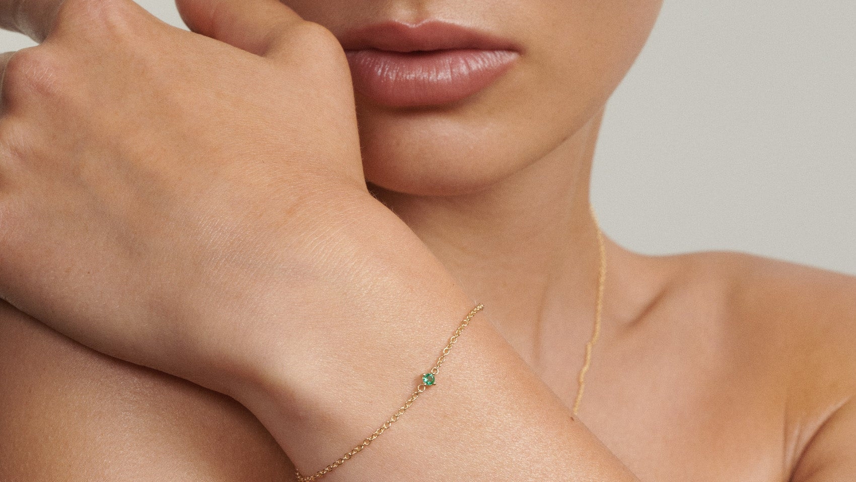 Woman wearing a gold bracelet with a green stone on a neutral background