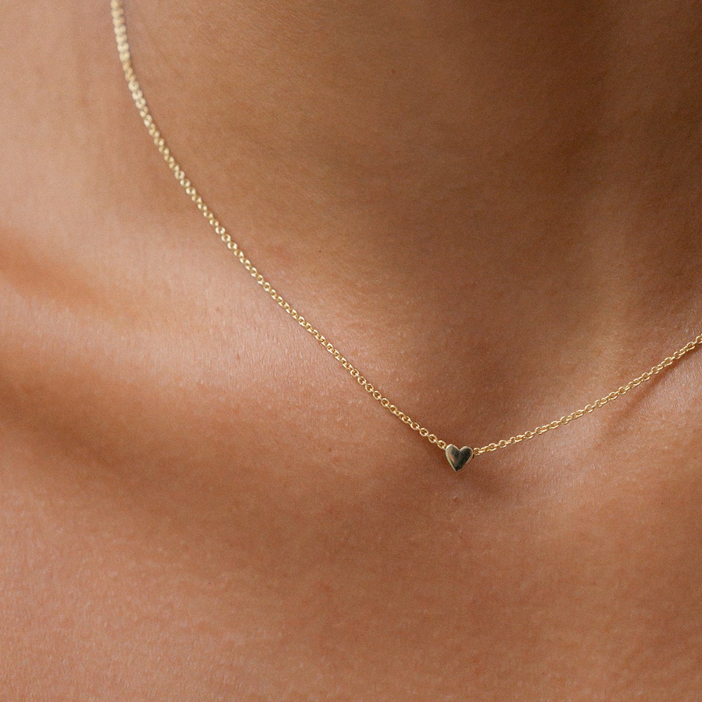 Gold necklace with a delicate heart pendant rests against a person's neck, exemplifying minimalist luxury jewellery.