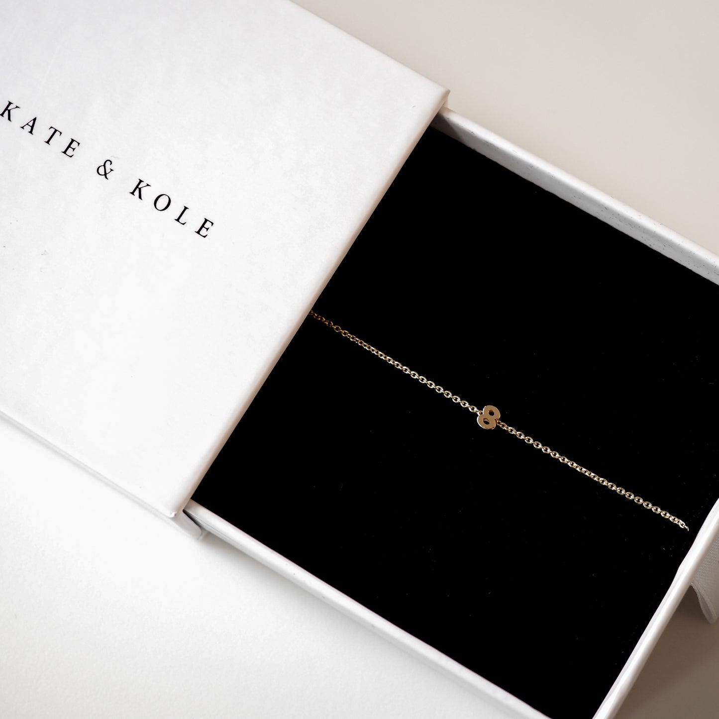 Delicate gold bracelet with a small charm in a white Kate & Kole box on a black velvet interior, embodying minimalist luxury jewellery.