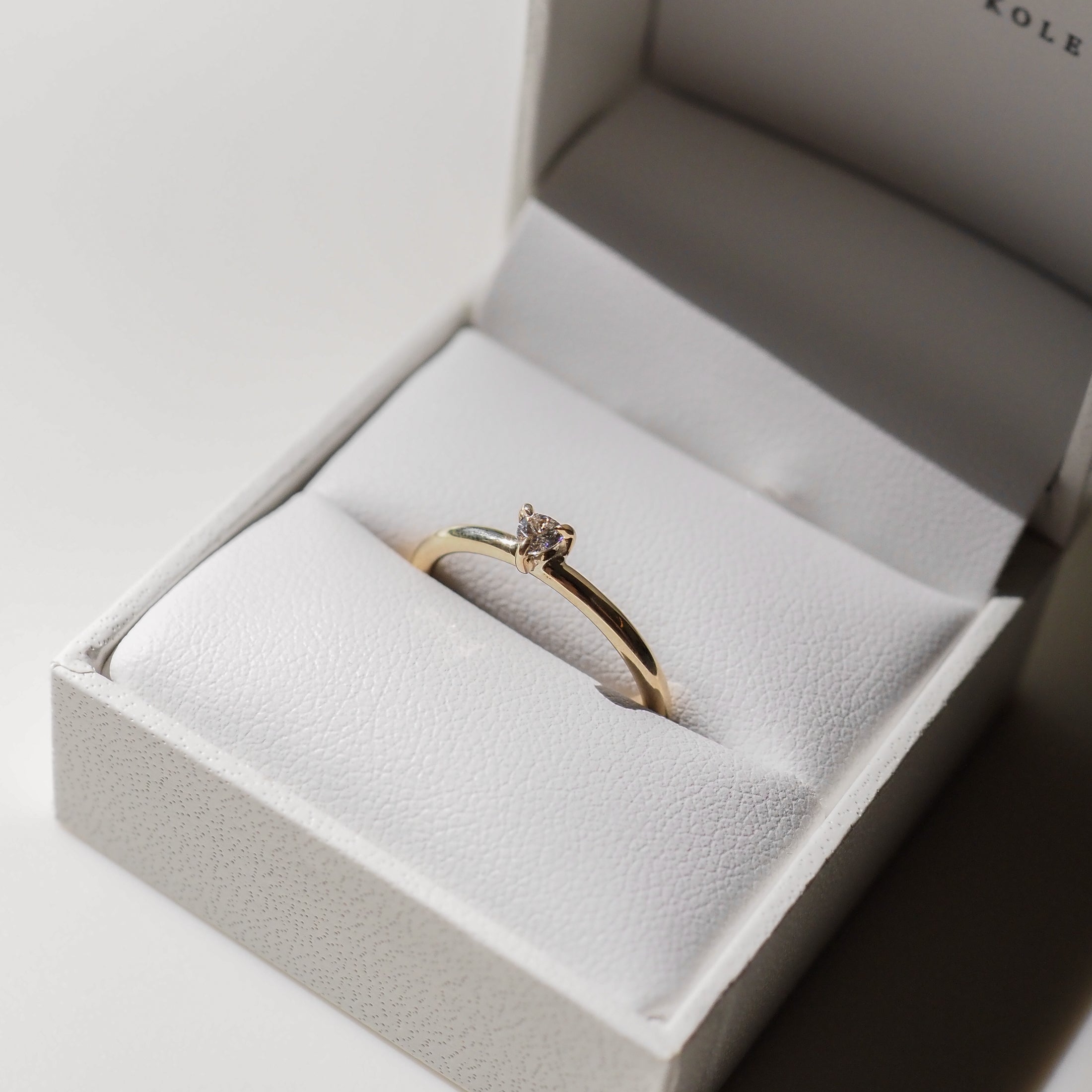 A gold engagement ring with a solitaire diamond in an open white jewellery box, showcasing elegant luxury.