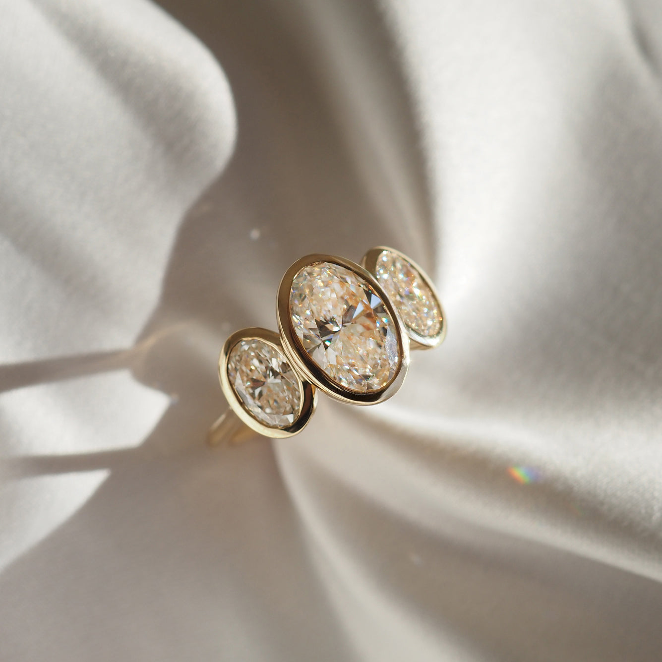 Gold ring with three oval diamonds on soft, elegant fabric background, capturing luxury jewellery aesthetics and sparkling brilliance.