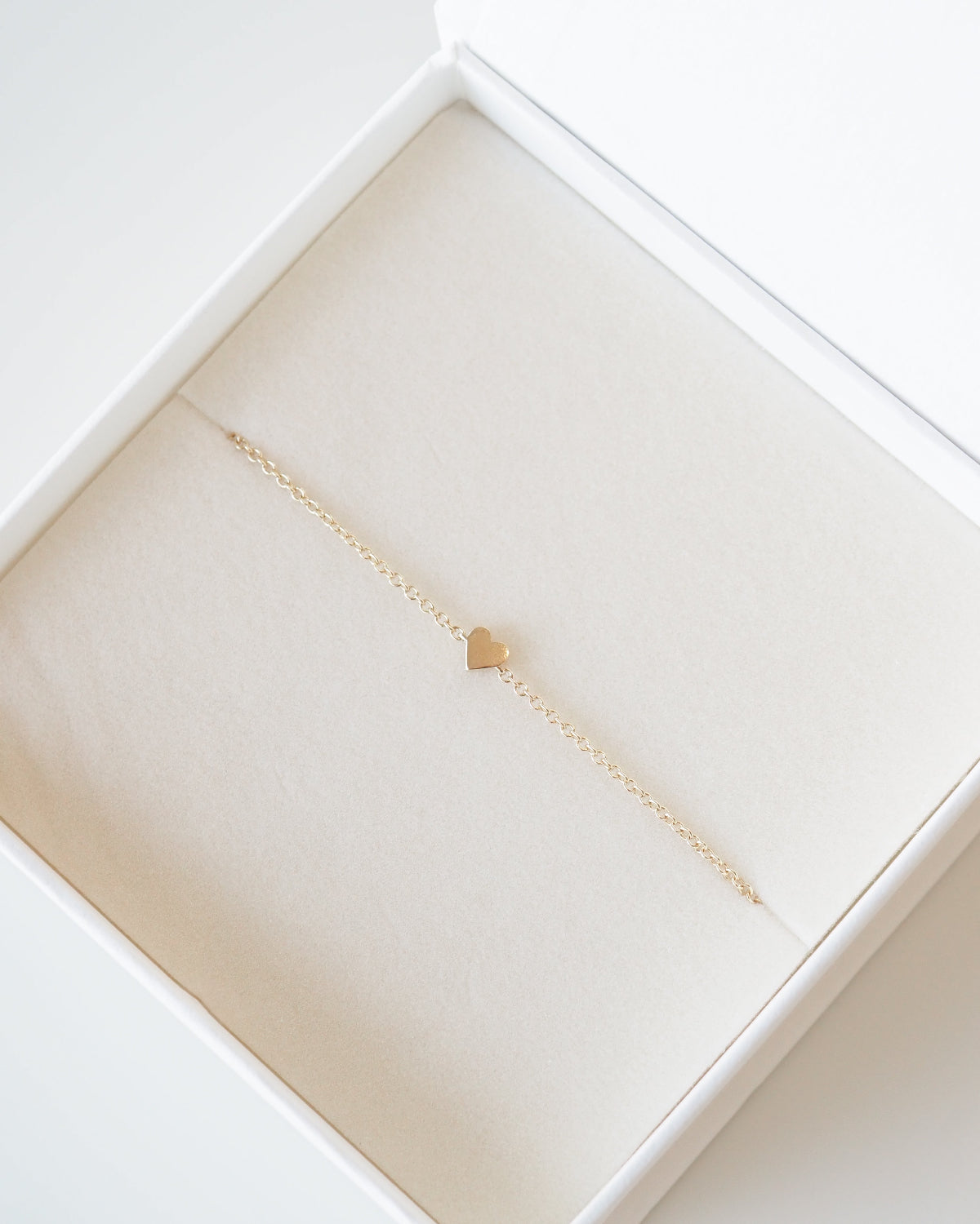 Gold necklace with a small heart pendant in a white jewelry box