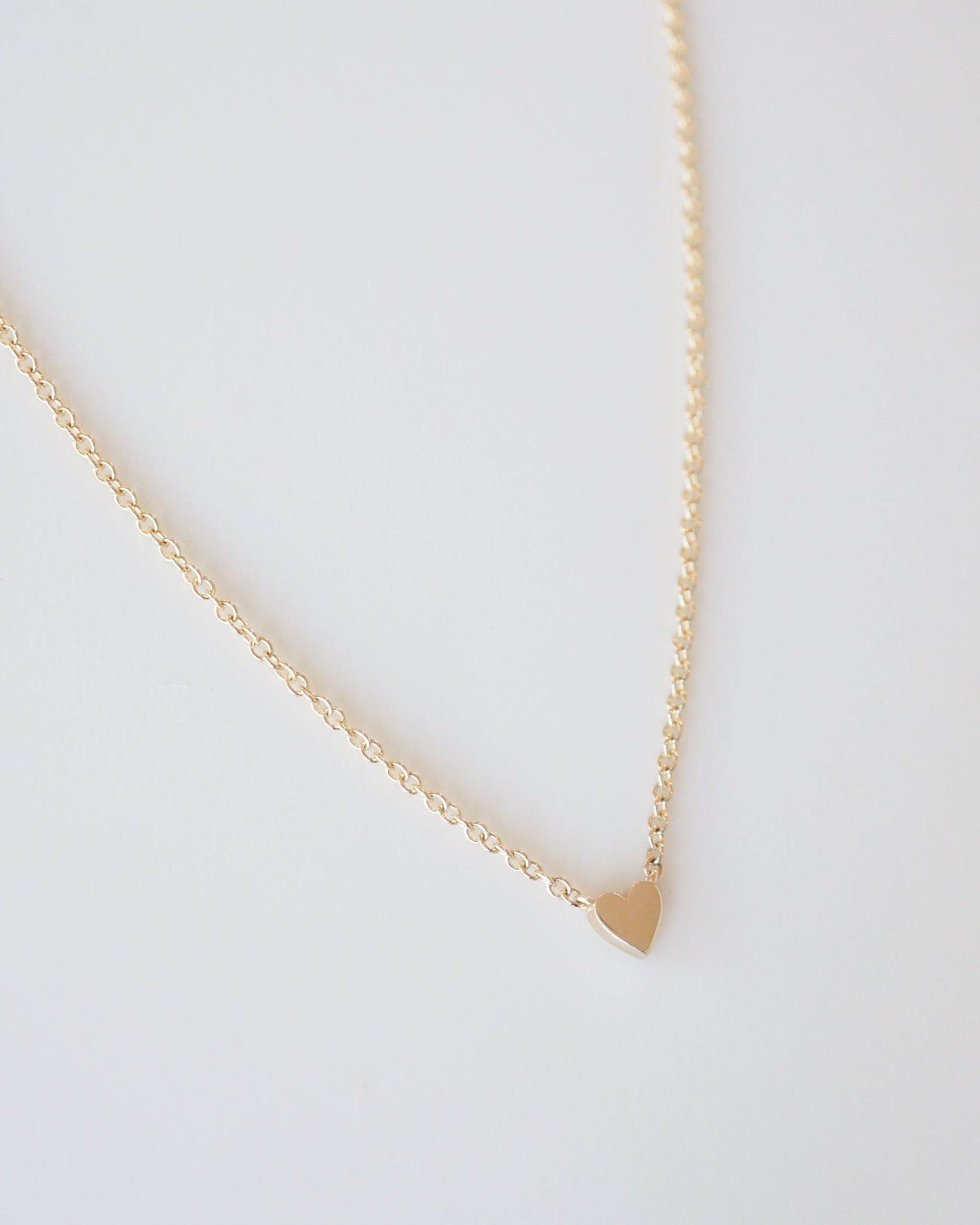 Gold necklace with a heart pendant on a light gray background